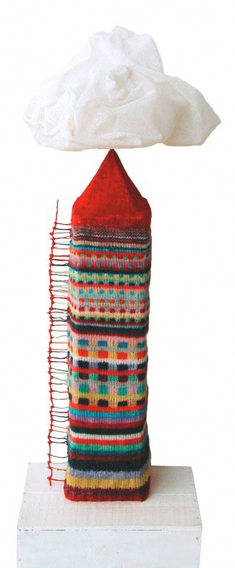 Turmförmiges Objekt mit bunt gestricktem Überzug, rotem Spitzdach und weisser Wolke obenauf, auf Sockel