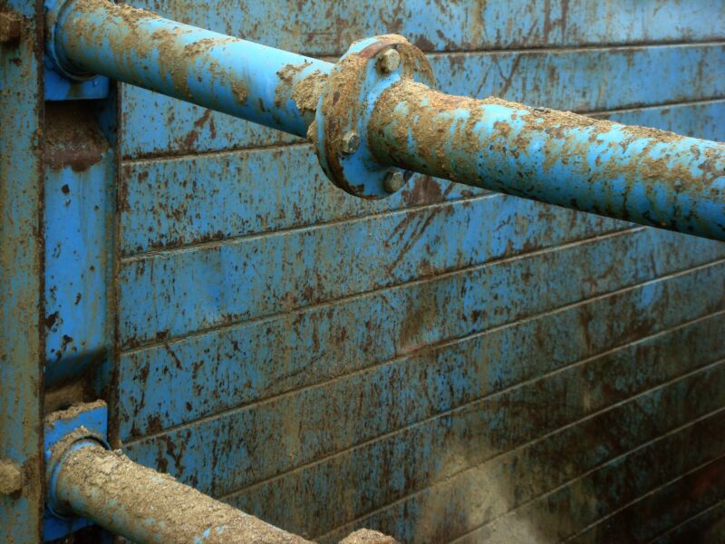 Verschmutzte blaue Rohre mit Flansch vor einer blauen, rostfleckigen Metallwand, Fotografie aus der Serie «Alltägliche Fundstücke II»