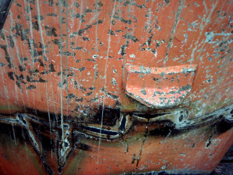 Orange Kunststoff- oder Metallfläche mit schwarzen Spritzern und hellen Laufspuren, Fotografie aus der Serie «Alltägliche Fundstücke II»