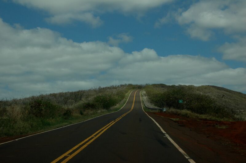 Gerade Landstrasse mit gelber Mittellinie steigt zwischen Buschhängen zu weissen Wolken an, Fotografie aus der Serie «Hawaii»