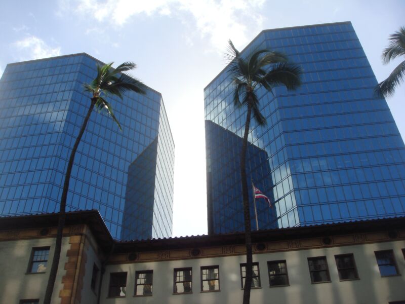 Zwei blau verglaste Bürotürme hinter einem flachen Altbau, davor zwei schlanke Palmen, Fotografie aus der Serie «Honolulu»