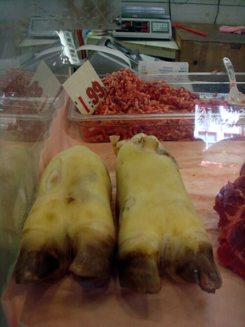 Zwei blassgelbe Schweinefüsse in einer Fleischtheke vor Hackfleisch mit Preisschild, Fotografie aus der Serie «Honolulu»