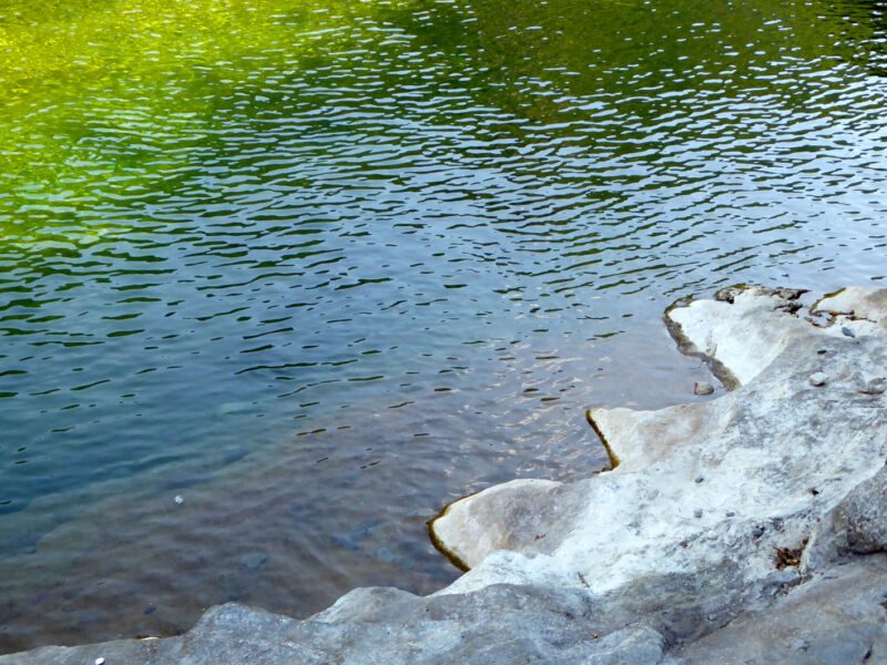 Blaugrüne, fein gekräuselte Wasserfläche an einer hellen, gezackten Felskante, Fotografie aus der Serie «An ligurischen Flüssen und Bächen»