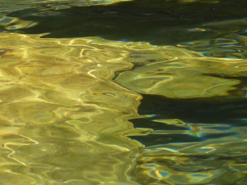 Abstrakte goldgelbe Lichtreflexe auf bewegtem Wasser mit dunklen Schattenzonen, Fotografie aus der Serie «An ligurischen Flüssen und Bächen»